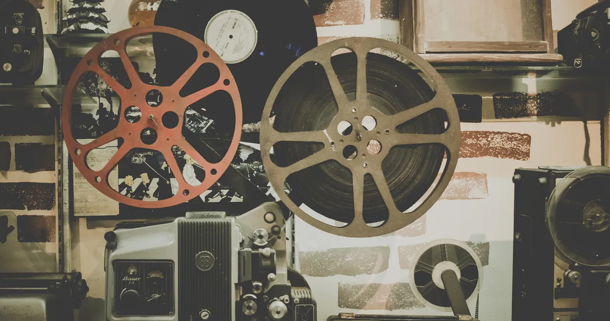 Bobinas de filme e projetores antigos sobre uma parede, ilustrando o teste de filmes no IPTV