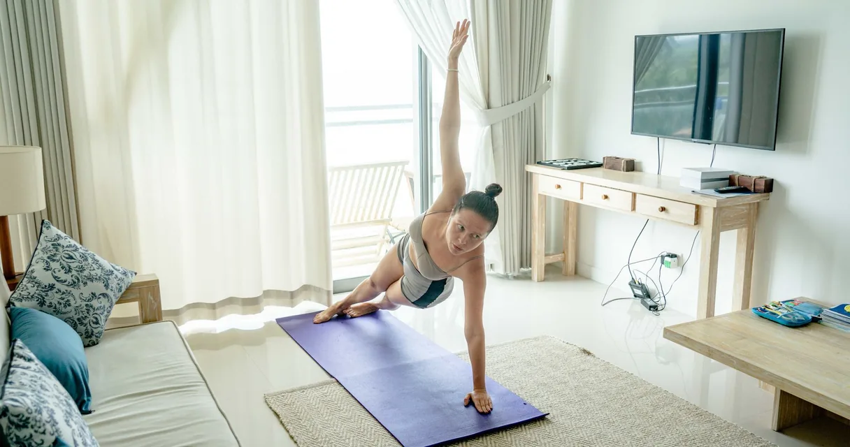 Mulher fazendo prancha lateral em um tapete no quarto de hotel, com a TV ao fundo